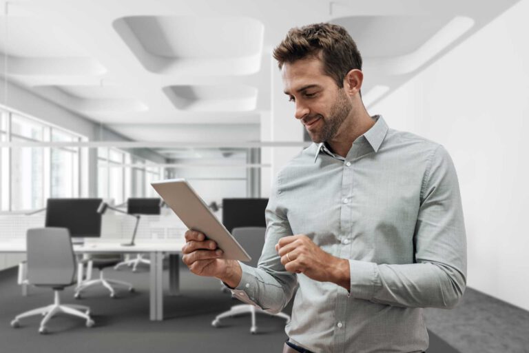 a man stands in an office and looks at a tablet
